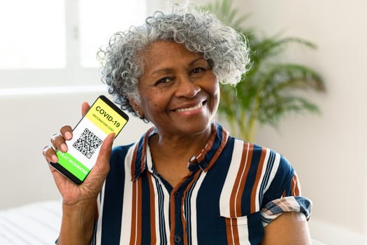 Happy senior african american woman showing covid vaccine passport on smartphone