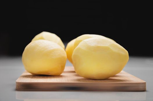 Close-up Several peeled potatoes on a wooden cutting board on a white table.