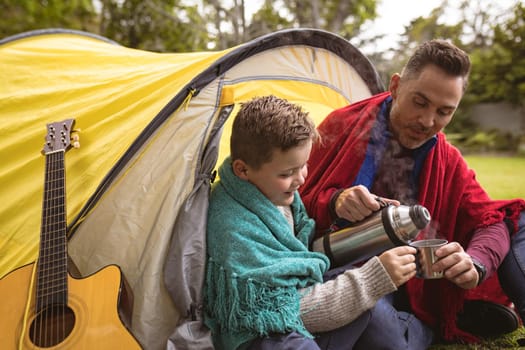 Caucasian father and pouring coffee in a cup for his son while sitting in a tent in the garden