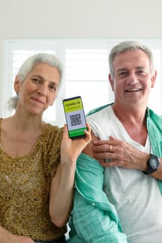 Smiling caucasian senior couple showing smartphone with covid vaccine passport on screen