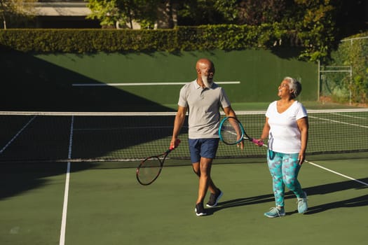 Portrait of smiling senior african american couple with tennis rackets on tennis court. retirement and active senior lifestyle concept.