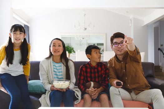 Excited asian parents with son and daughter sitting on couch watching tv with popcorn