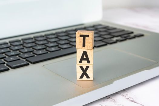 Tax text on wooden block cube placed on laptop or notebook. Tax concept.
