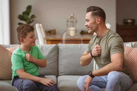 Caucasian father and son communicating using sign language while sitting on the couch at home