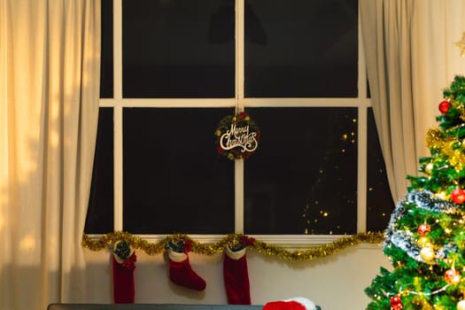 Composition of merry christmas sign in window, with christmas stockings and christmas tree