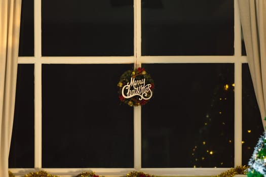 Composition of merry christmas sign with decorations hanging in window at night