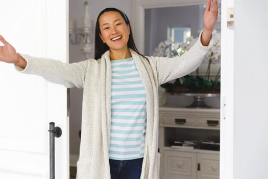 Portrait of smiling asian woman with arms wide greeting visitor at door