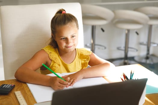 Caucasian girl sitting at table and using laptop during online lessons
