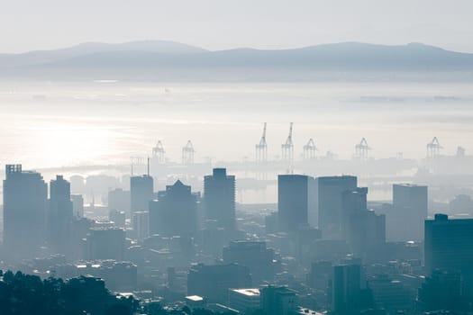 General view of cityscape with multiple modern buildings and cranes in the foggy morning