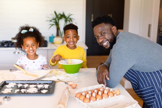 Happy african american father and siblings baking together in kitchen
