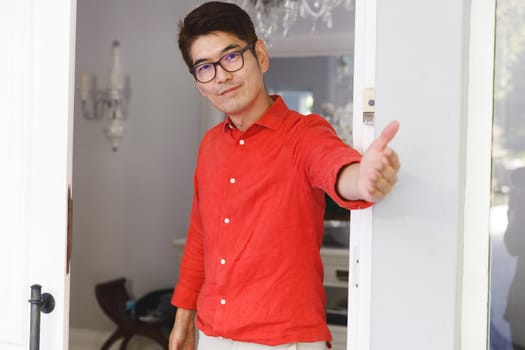 Portrait of smiling asian man standing at door and inviting visitor to room