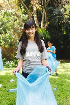 Portrait of smiling asian daughter putting rubbish in refuse sacks with family in the countryside