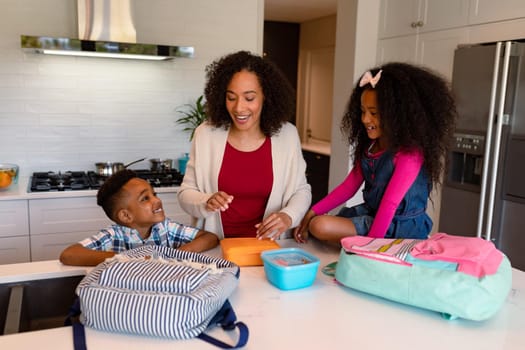 Happy african american mother and children preparing lunchboxes for school
