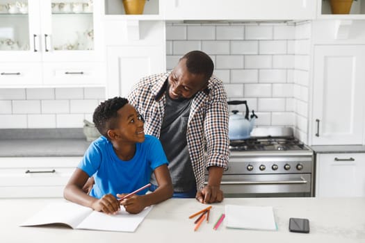 Smiling african american father and his son in kitchen, doing homework together. family spending time at home.