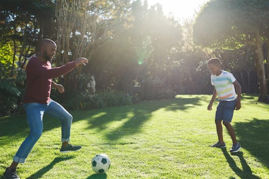 African american father with son having fun and playing football in garden. family spending time at home.