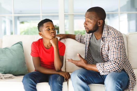 African american son sitting on couch listening to father talking in living room