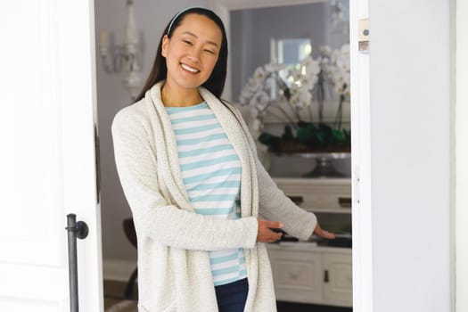 Portrait of smiling asian woman standing at door and inviting visitor to room