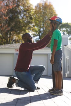 African american father with son smiling and preparing before skateboarding in garden. family spending time at home.