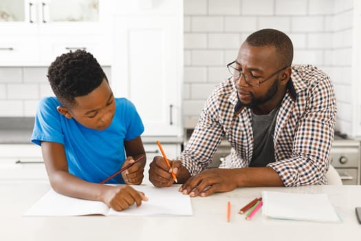 African american father and his son in kitchen, doing homework together. family spending time at home.