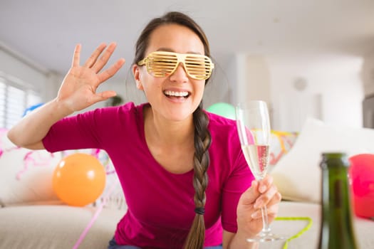 Happy asian woman raising champagne glass making new year's eve laptop video call