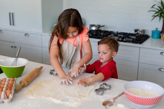 Focused caucasian siblings baking together, making cookies in kitchen