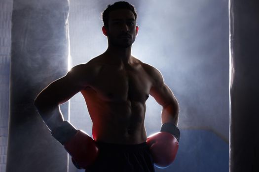 Im fight ready. Cropped portrait of a silhouetted young male boxer standing with his hands on his hips after a workout on the punching.