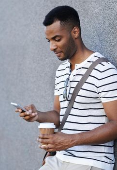 Arranging a meeting. A handsome african american businessman leaning against a wall in the city while using his mobile.