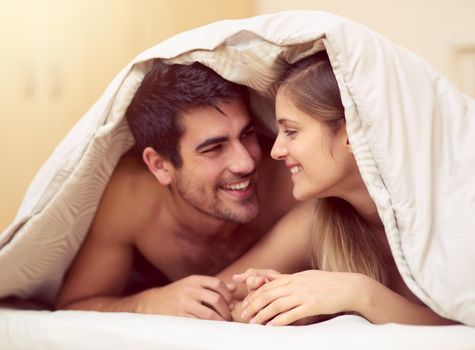 Love the one youre with. Shot of a loving young couple smiling at each other while lying under a blanket together.
