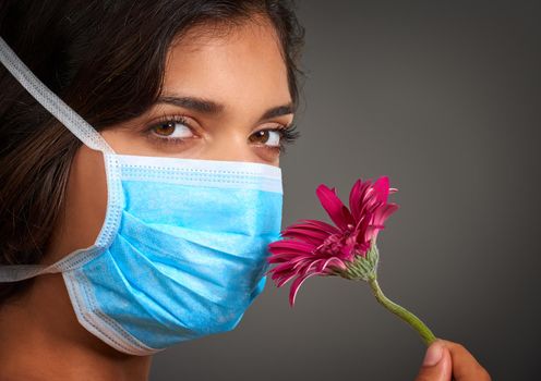 I cant seem to smell anything. Closeup of a young woman with a doctors mask on looking at the camera and smelling a flower.