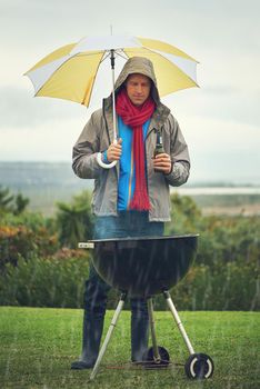 Real men bbq anytime. Shot of a man barbecuing in the rain.
