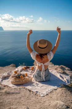 Street photo of a beautiful woman with dark hair in a white top, shorts and a hat having a picnic on a hill overlooking the sea