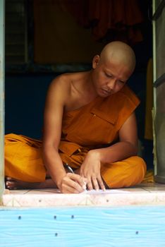 Penning down some deep thoughts. Shot of a buddhist monk filling in a form while sitting in the doorway of his home.