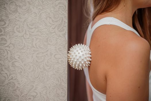Athletic slim caucasian woman doing thigh self-massage with a massage ball indoors. Self-isolating massage