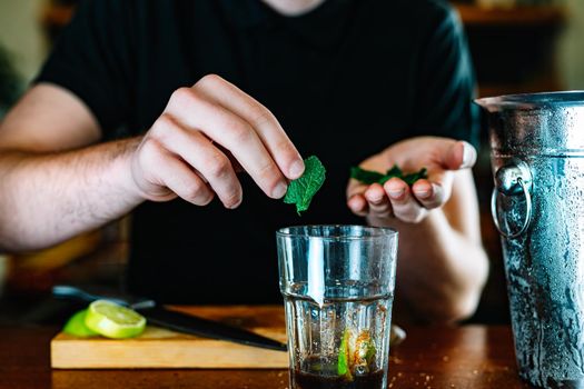 detail of the hands of a young and modern waiter, adding mint in the preparation of a mojito.