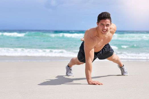 Getting stronger with each rep. Portrait of a handsome young man doing one handed pushups on the beach.