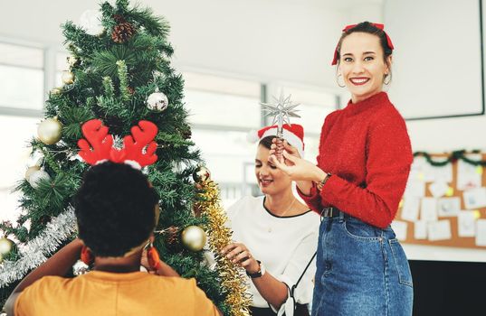 A Christmas tree isnt complete without the shining star. Portrait of an attractive young businesswoman decorating a Christmas tree with her colleagues at work.
