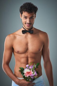 Ive got the bow and flowers, lets get married. Studio shot of a handsome young shirtless man posing against a grey background.