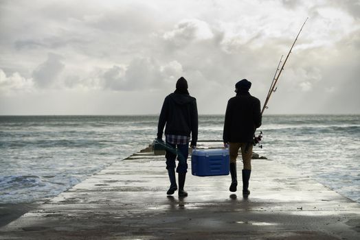 Carrying home their catch. Shot of two young men fishing at the ocean in the early morning.