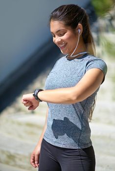Making great progress. Shot of a young woman checking her watch while out exercising.
