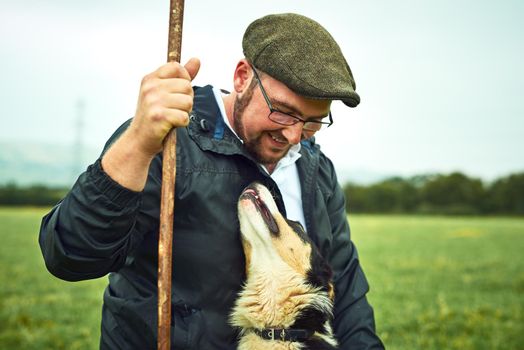 My best friend and I. Shot of a cheerful young farmer and his dog looking at each other while standing on a green field on the farm.