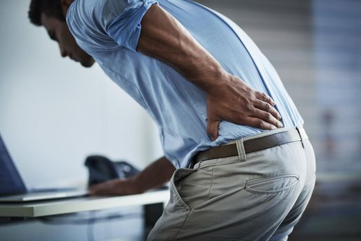 Its so painful I cant even stand up properly. Shot of a young businessman suffering with back pain at work.