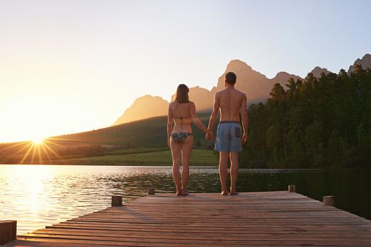 Time for a sunset dip. Rearview shot of a young couple in swimsuits standing on a dock at sunset.
