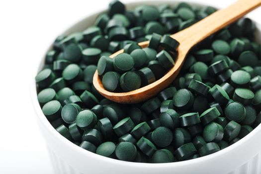 Organic spirulina tablets in a white cup with a wooden spoon