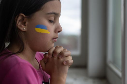 Little girl with Ukrainian flag ribbon praying. Symbol of peace and pray for Ukraine.