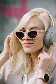 Portrait of blonde woman in headphones listening music with sunglasses. model wear stylish wireless headphones enjoy listen new cool music.
