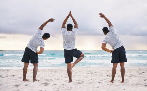 Rearview shot of three unrecognizable male athletes practicing yoga on the beach.