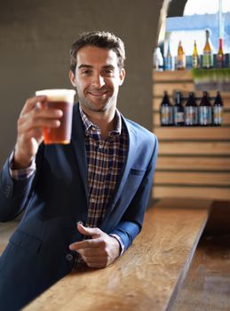 Cheers to you. Shot of a handsome young man enjoying an ale at the bar.