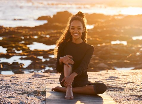Shot of an attractive young woman sitting on her yoga mat during a yoga session on the beach at sunset.