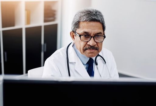 I have my work cut out for me today. Cropped shot of a focused mature male doctor working on a computer while being seated in his office during the day.