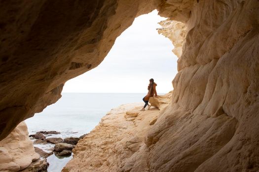 view from a cave to a sea with a girl sitting on a stone